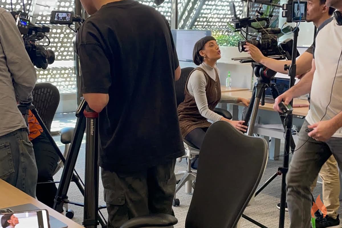 Film crew shooting a scene with an actor at a desk in a modern office