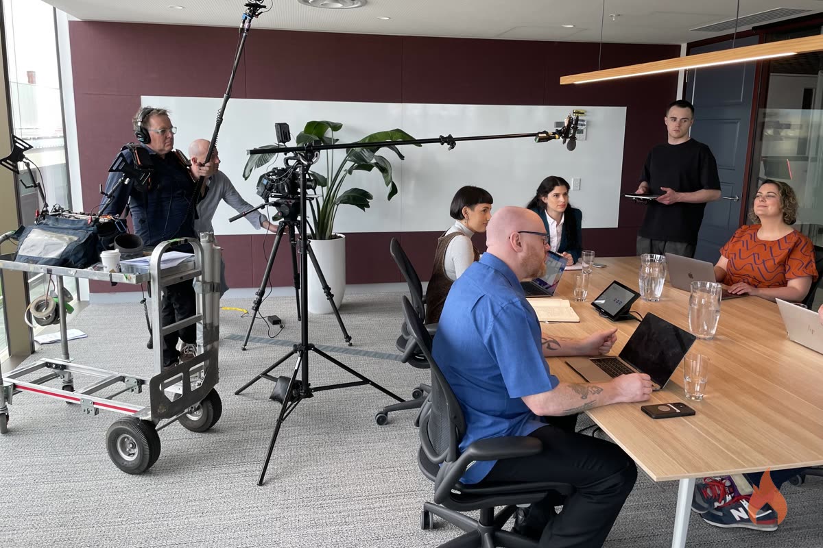Full film set in a boardroom with boom mic, dolly and cast around the table
