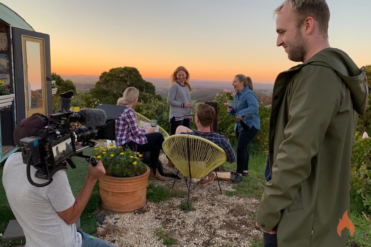 Camera operator filming a group scene outdoors at sunset