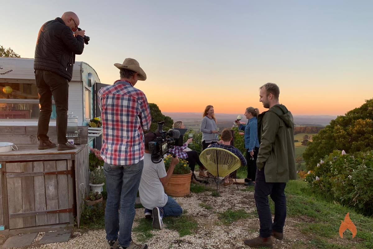 Crew shooting beside a caravan at dusk, photographer standing on a bench